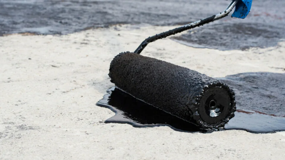 Bituminous coating being roller-applied to a flat roof